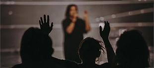 Membros da plateia levantando as mãos durante uma apresentação